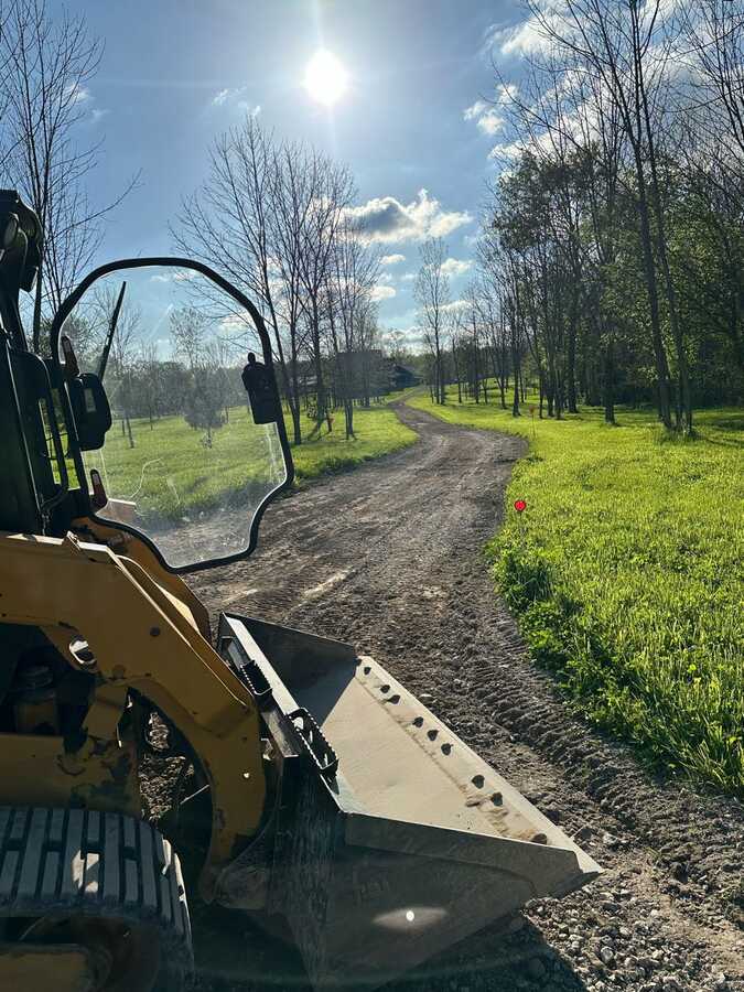 Skid steer grading a long gravel driveway