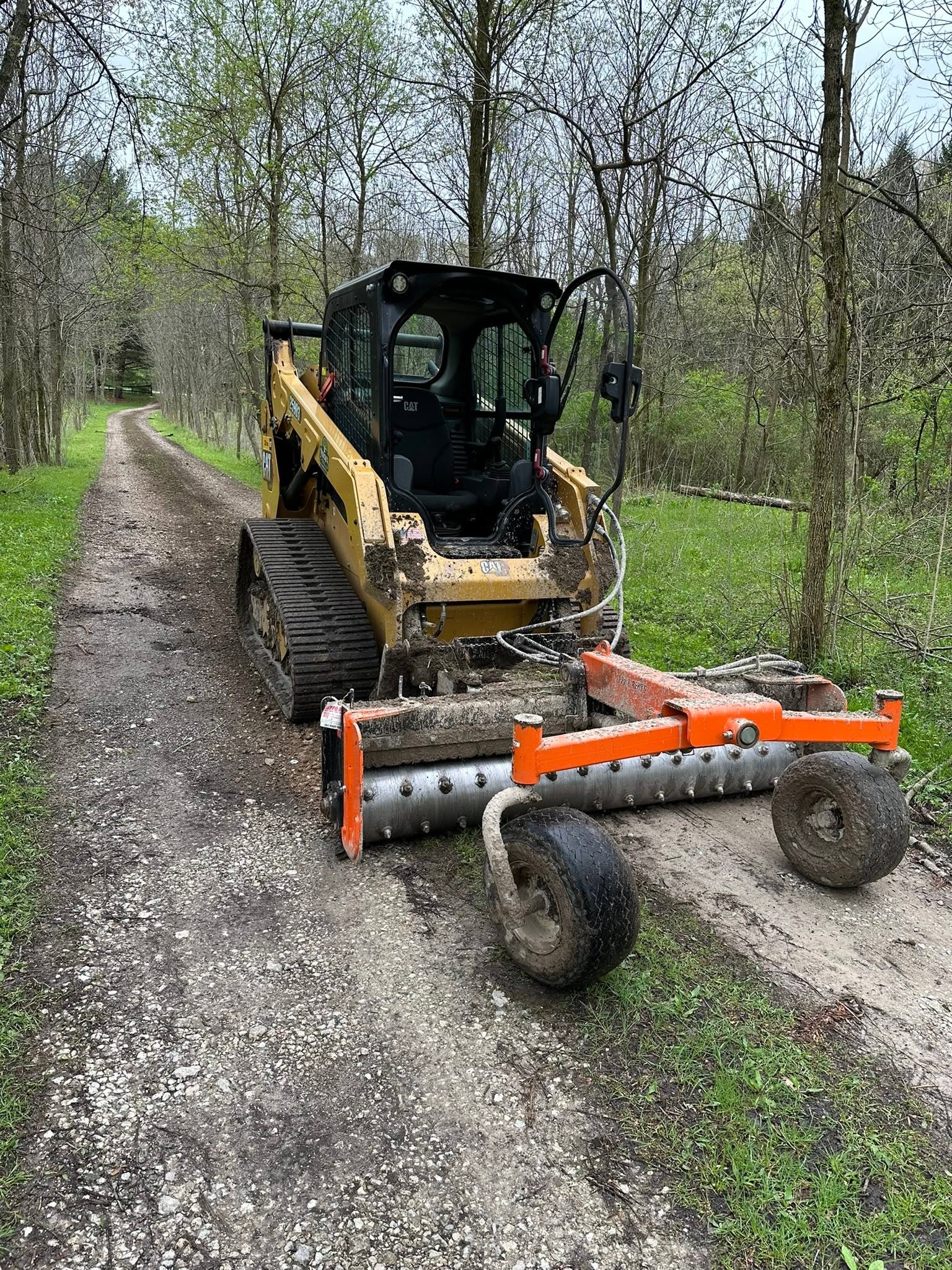 Tracked skid steer with grading attachment working on a gravel driveway
